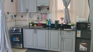A compact kitchen with white cabinets, a stove, a microwave, and a sink. - Stunning Studio Apartment on Entebbe that is fully furnished and accessible (Namulanda)