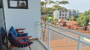 A balcony with a red chair and a white railing overlooking a street with buildings and trees. - Stunning Studio Apartment on Entebbe that is fully furnished and accessible (Namulanda)