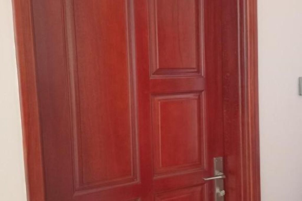 Puerta de madera roja cerrada con picaporte y cerrojo de metal.