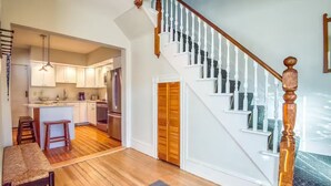 A spacious kitchen with white cabinets, a wooden dining table, and a staircase with white balusters. - Home in Heart of Downtown North Conway (Conway)
