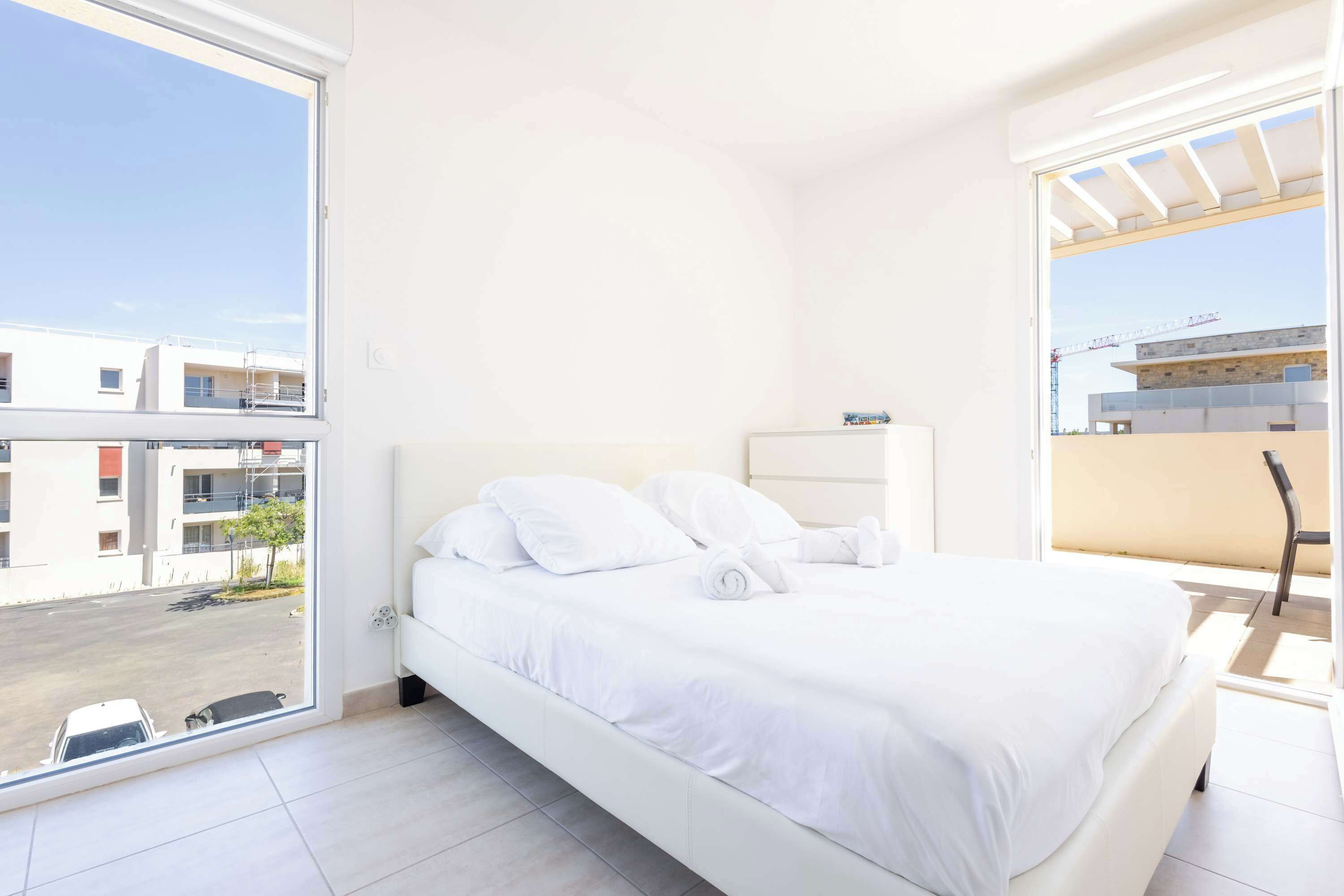 Un dormitorio con un ventanal grande, una cama y vistas a edificios.