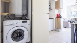 A modern kitchen with a washing machine, wooden cabinets, and a dining area.
