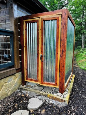 Un abri en bois avec une porte en métal, construit sur des fondations en pierre et accessible par un petit marchepied.