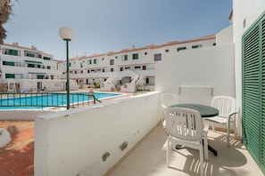 A rooftop terrace with a swimming pool, white walls, and a table with chairs.