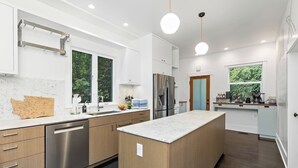 A modern kitchen with a central island, stainless steel appliances, and a view of greenery outside. - Broadway & Bloom | Luxe Stay (Seattle)