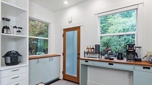A modern kitchen with white cabinetry, a built-in oven, a coffee maker, and a window with a view of trees. - Broadway & Bloom | Luxe Stay (Seattle)