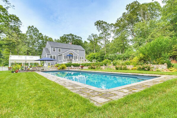 A large house with a swimming pool, surrounded by lush greenery and a white fence. - Pool, Sunroom & Gardens: Luxe Sandy Hook Home! (Sandy Hook)