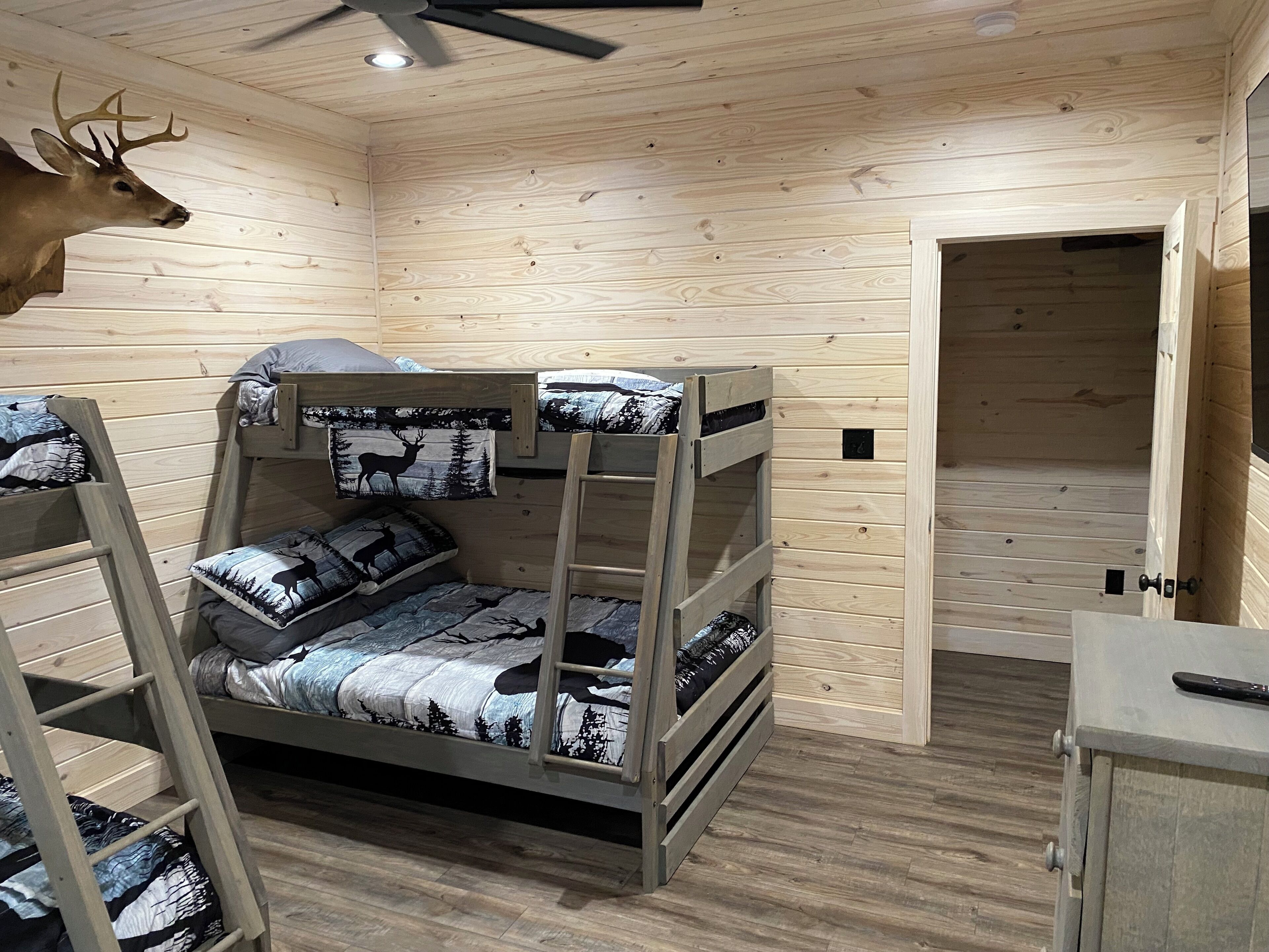 Ein Schlafraum mit Etagenbetten, einer Dekoration mit Hirschgeweih, Holzwänden und einem Deckenventilator.