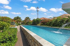 A swimming pool with a stone wall, surrounded by lush greenery and a clear blue sky. - Casa Sirena — Your Peaceful Curaçao Hideaway (Willemstad)