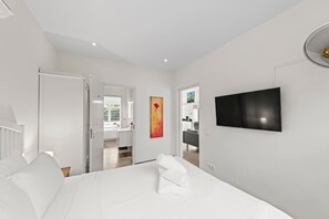 Et moderne hotelværelse med en stor seng, et fladskærms-tv og en dør til et badeværelse.