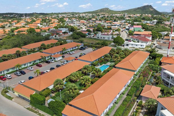 A residential area with multiple buildings, a swimming pool, and a hilly background.