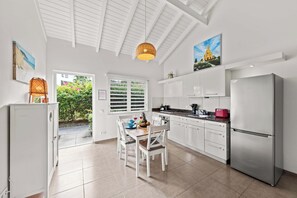 A modern kitchen with white cabinets, a stainless steel refrigerator, and a dining area with a table and chairs. - Casa Sirena — Your Peaceful Curaçao Hideaway (Willemstad)