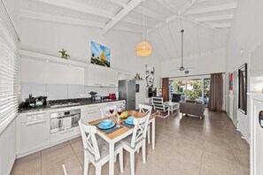 A modern kitchen with white cabinets, a wooden dining table, and a large window. - Casa Sirena — Your Peaceful Curaçao Hideaway (Willemstad)