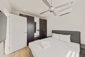 A modern hotel room with a bed, a ceiling fan, an air conditioning unit, and a wardrobe.