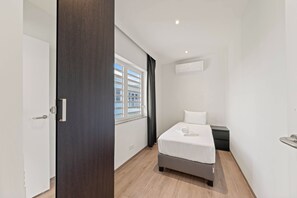 Ein modernes Schlafzimmer mit einem Bett, einem Fenster mit Jalousien, einer Tür und einer Wand-Klimaanlage.