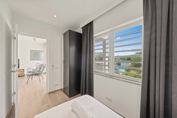 A modern hotel room with a large window, a bed, a wardrobe, and a view of a pool.