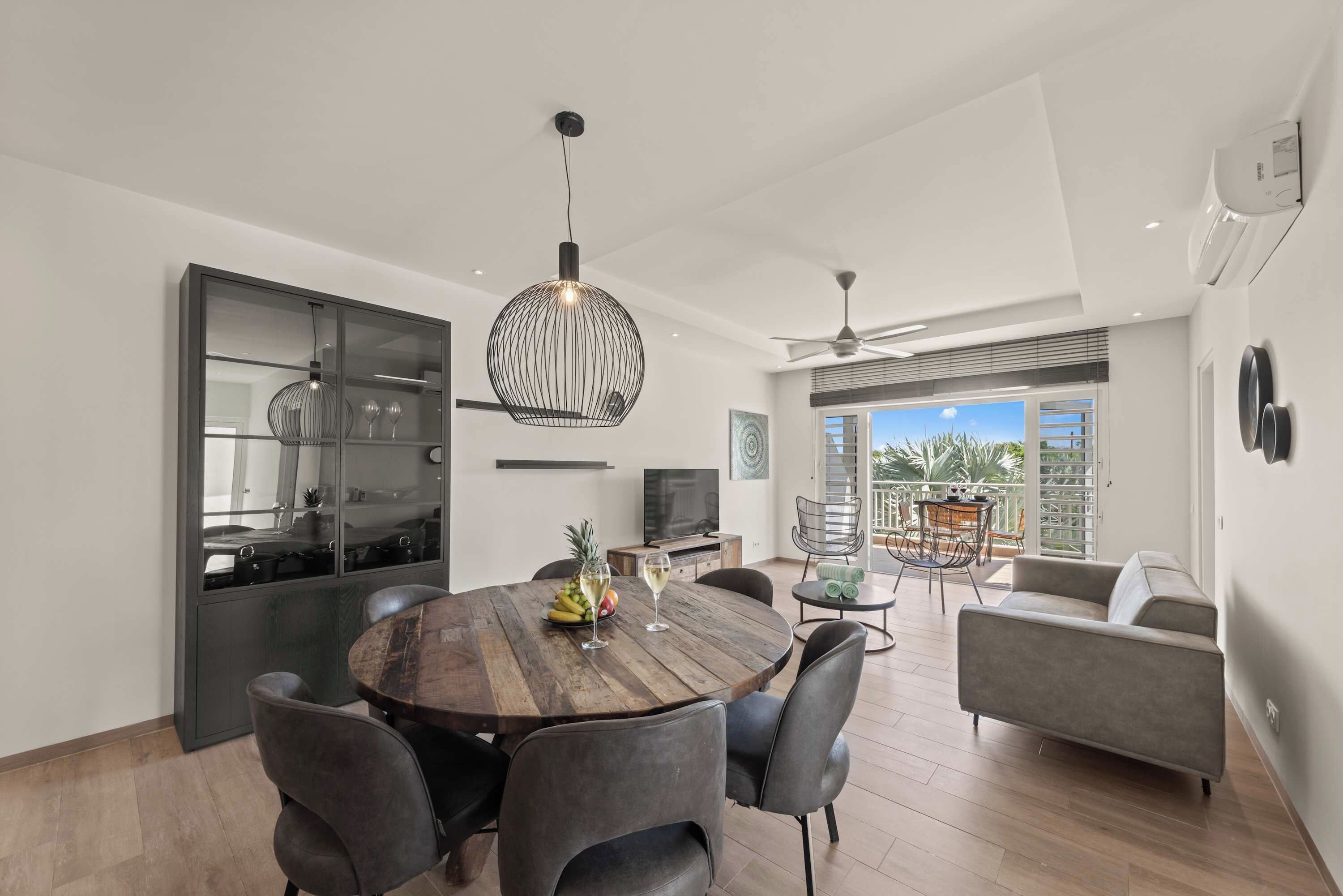 A modern dining area with a wooden table, dark chairs, and pendant lighting.