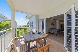 An outdoor patio with a wooden table and chairs, a glass door leading to an interior space, and a view of a residential area.