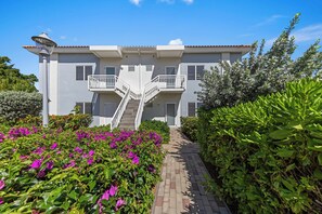 A two-story building with a central staircase, surrounded by well-maintained gardens and hedges.