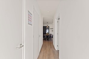 A hallway leading to a dining area with a table and chairs, a hanging light fixture, and a framed notice on the wall.
