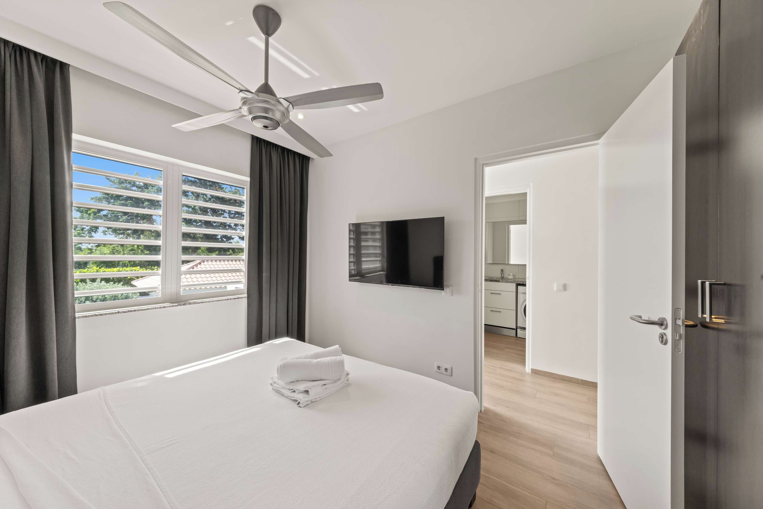 A hotel room with a bed, a ceiling fan, a flat-screen TV, and a view of the outside.