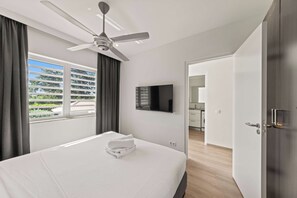 A hotel room with a bed, a ceiling fan, a flat-screen TV, and a view of the outside.