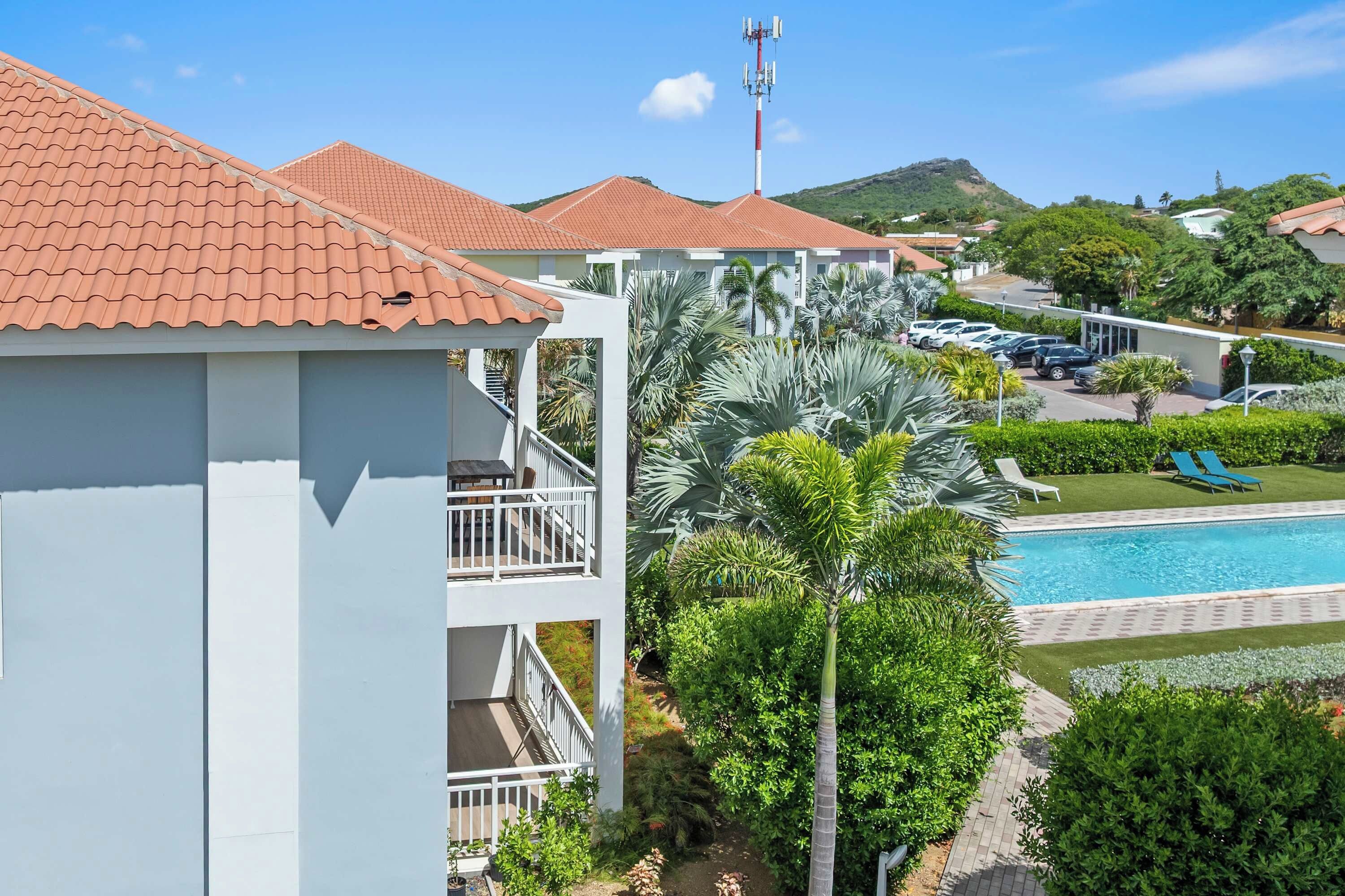 A hotel with a swimming pool, palm trees, and a view of a hilly landscape.