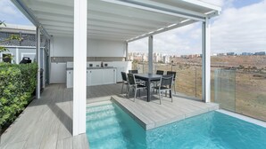 Ett modernt utomhuskök med pool, matplats och utsikt över staden.