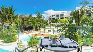 A poolside table with a breakfast setup, surrounded by lush greenery and a clear blue sky. - Warm Studio Lagoon View CPL D202 (Tulum)