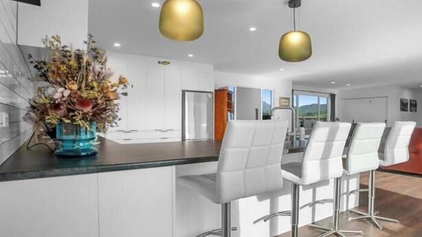 A modern kitchen with white cabinetry, a central island with bar stools, and two pendant lights.