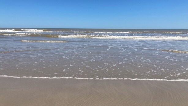 A beach with waves gently lapping at the shore under a clear blue sky.