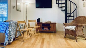 A living room with a TV, a wooden table with chairs, a wicker chair, and a spiral staircase.