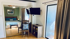 A hotel room with a bed, a desk with a chair, a television, and a sliding glass door.