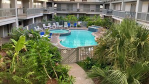 An indoor swimming pool with multiple levels of balconies, surrounded by lush greenery and various seating areas.