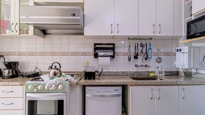 A kitchen with white cabinets, a stove, a dishwasher, and various kitchen utensils. - Apto Pet-friendly com Garagem e Vista de Botafogo (Rio de Janeiro)
