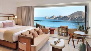 A modern bedroom with a large bed, a sofa, a dining table, and a view of the sea. - Corazon Cabo Resort & Spa - Oceanfront infinity pools, beach club, rooftop bar, (Cabo San Lucas)