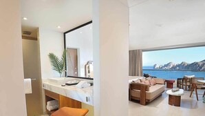 A modern bathroom with a vanity, a sink, and a mirror. Adjacent to the bathroom is a living area with a sofa, a coffee table, and a view of the sea. - Corazon Cabo Resort & Spa - Oceanfront infinity pools, beach club, rooftop bar, (Cabo San Lucas)