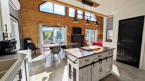 A modern kitchen with wooden walls, a central island, and pendant lighting. - Cozy River Lodge Chalet - AC - Hot Tub - Waterfront - Pet Friendly (Saint-Côme)