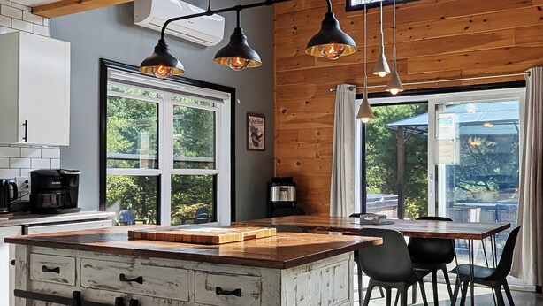 A modern kitchen with a rustic island, pendant lighting, and large windows. - Cozy River Lodge Chalet - AC - Hot Tub - Waterfront - Pet Friendly (Saint-Côme)
