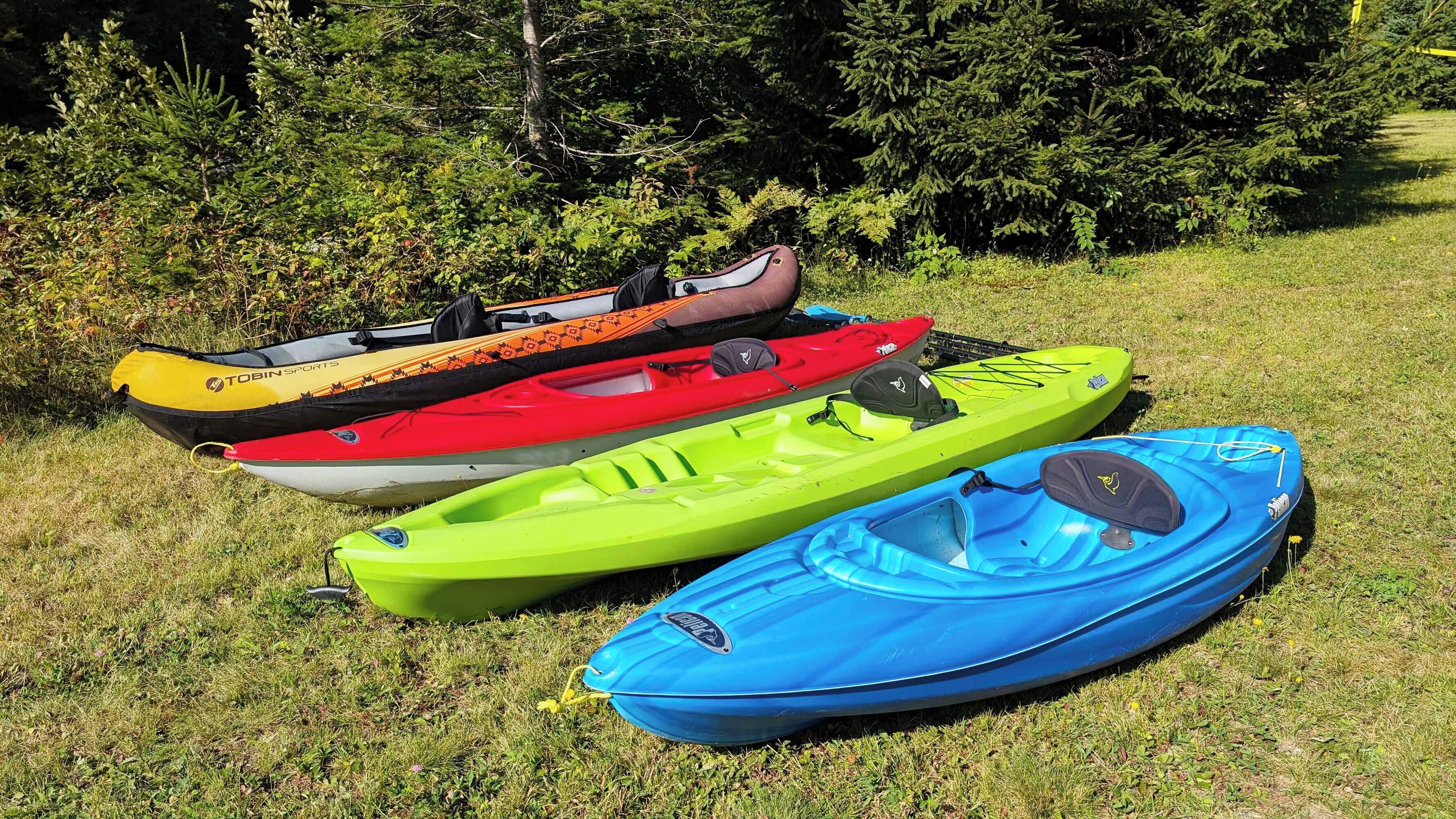 Four kayaks on a grassy area with dense foliage in the background.