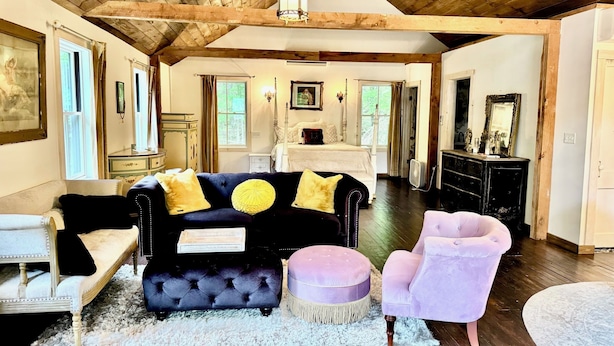 Ein geräumiges Wohnzimmer mit einem dunkelblauen Sofa, einem weißen Bett und einer Holzbalkendecke.