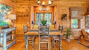 A wooden cabin interior with a dining table, chairs, a chandelier, and a fireplace. - Secluded 3 Bedroom Cabin w/hot tub in the mountains of Clayton, Ga (Clayton)