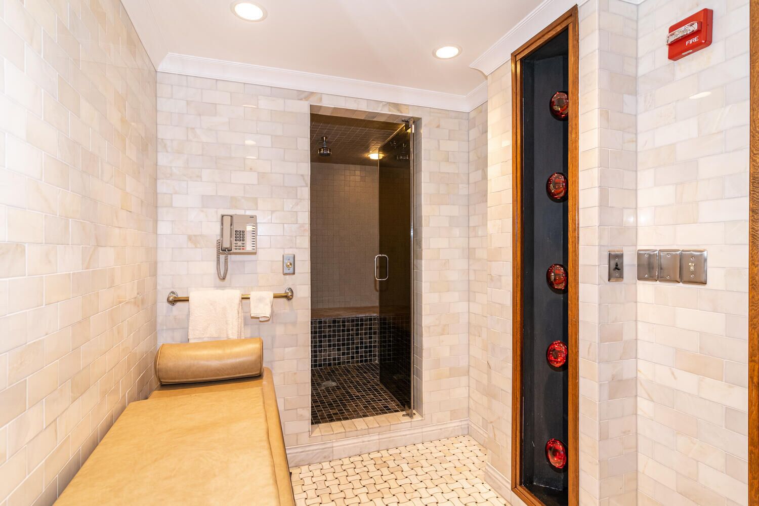 A modern bathroom with a shower, a towel rack, a telephone, and a fire alarm.