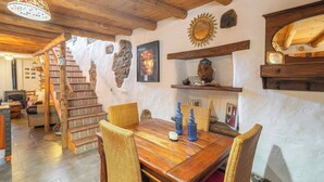 A rustic interior with a wooden staircase, wicker chairs, a wooden dining table, and stone walls. - La Pelotilla Genalguacil by Ruralidays (Málaga)