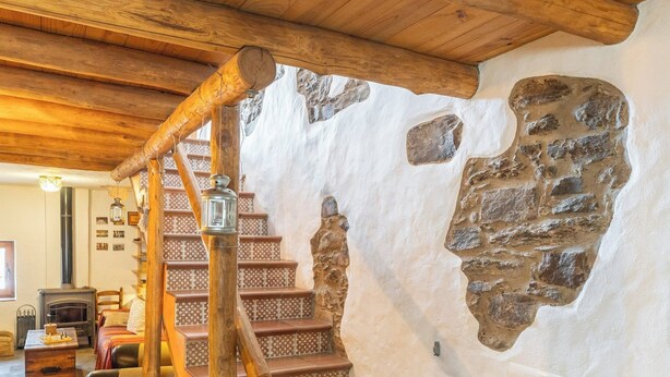 A rustic interior with a wooden staircase, stone wall, and a fireplace. - La Pelotilla Genalguacil by Ruralidays (Málaga)
