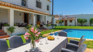 A poolside dining area with a table set for two, a vase with flowers, and a bowl of lemons.