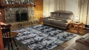 Ein gemütliches Wohnzimmer mit einem Stein-Kamin, einem Ledersofa, einem Holztisch und einer rustikalen Holzbalkendecke.