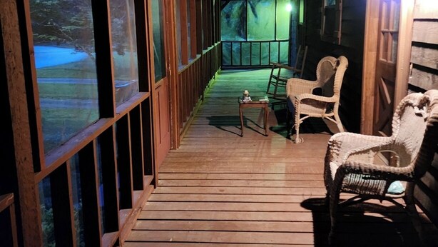 Eine hölzerne Veranda mit Blick auf eine verschneite Landschaft, zwei Korbstühle und ein kleiner Tisch.