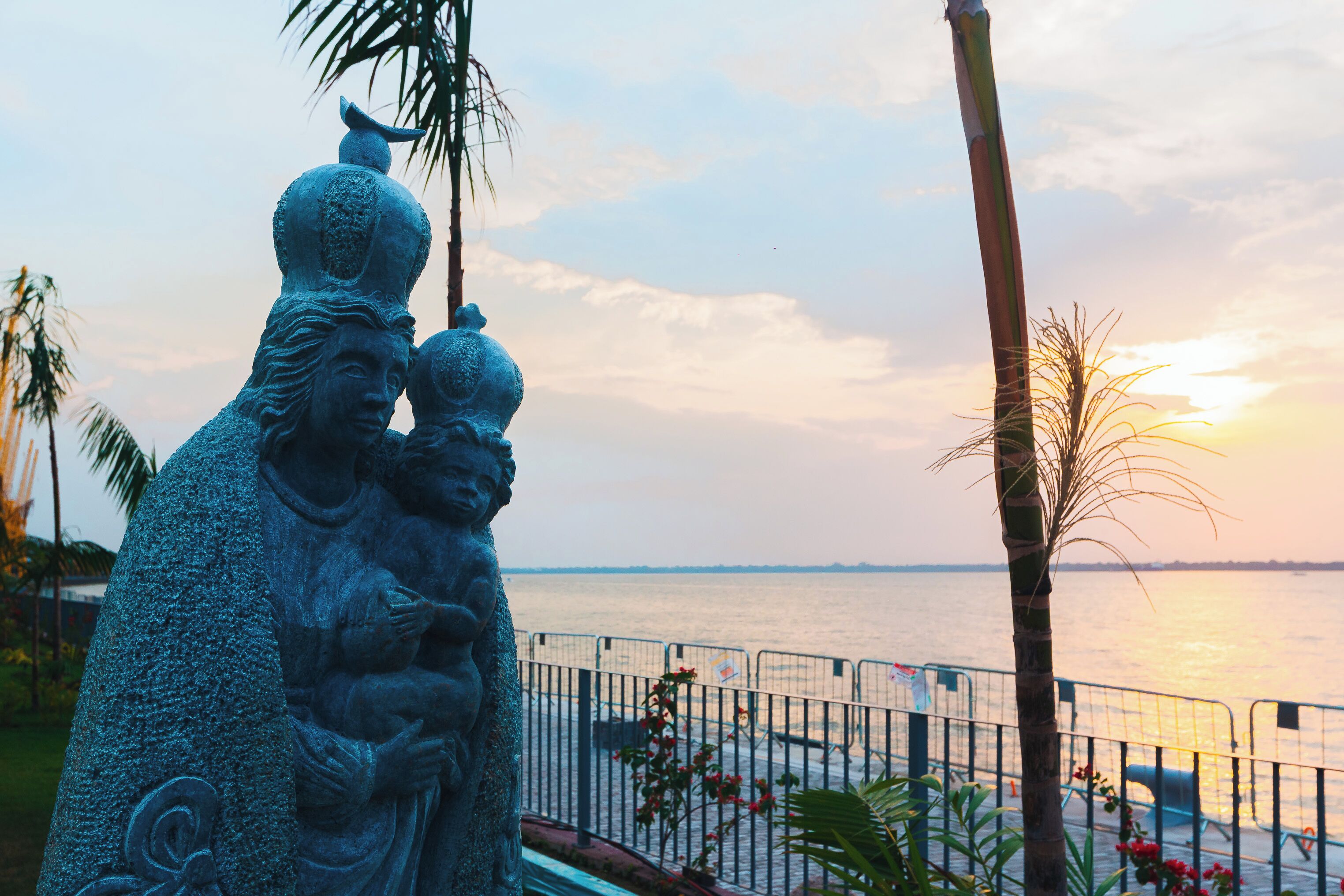 A statue of a family by a waterfront with a fence in the foreground.
