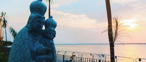 A statue of a family by a waterfront with a fence in the foreground.